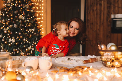 Cheerful parents and a child in red pajamas prepare christmas cookies in the decorated kitchen