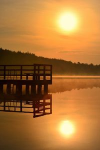 Silhouette gazebo by lake against sky during sunset