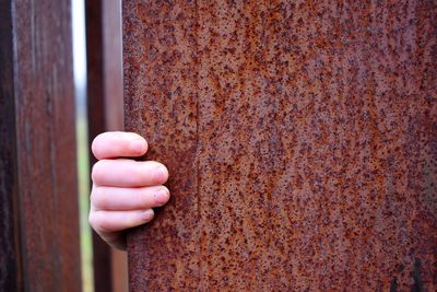 Close-up of hand holding rusty metal against wall