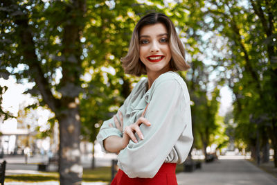 Portrait of smiling young woman standing against trees