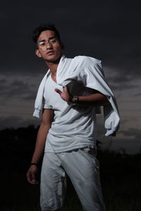 Portrait of young man holding jacket standing against sky