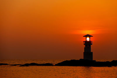 Lighthouse by sea against orange sky