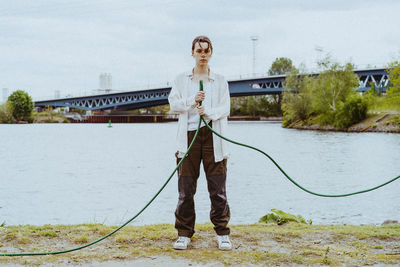 Full length portrait of confident young non-binary person holding garden hose