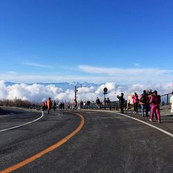 People walking by road against blue sky