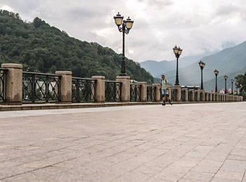 Young man in protective equipment riding on roller skates along embankment against  forest mountains