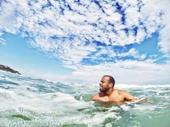 Man looking away while swimming in sea against sky