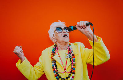 Portrait of woman wearing sunglasses against orange background