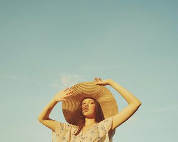 Portrait of young woman wearing hat standing against sky