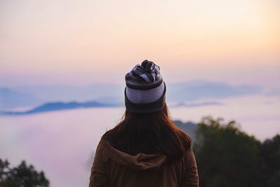 Rear view of woman looking at lake against sky during sunset