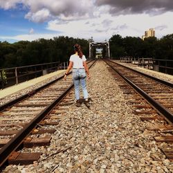 Woman walking on railroad tracks against sky