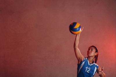 Full length of a woman holding ball against wall