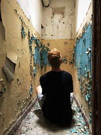 Rear view of man sitting in abandoned building