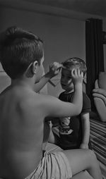 Shirtless boy adjusting brother hair at home