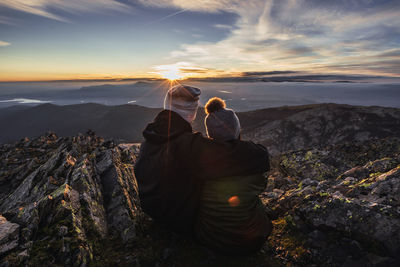 People on rock against sky during sunset