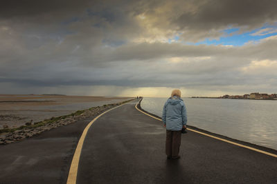 Rear view of boy standing on road against sky