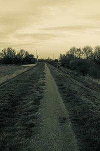 Road amidst field against sky during sunset