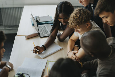 Smiling teenage girl and boys with non-binary person discussing with male teacher at desk