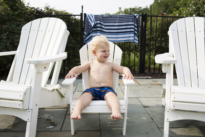 Happy shirtless boy sitting on chair in backyard