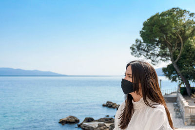 Portrait of young woman with protective face mask on sea shore.