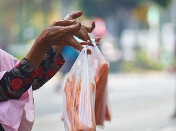 Cropped hands of woman holding vegetables in plastic bags