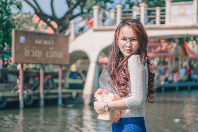 Portrait of young woman standing against river and text on board