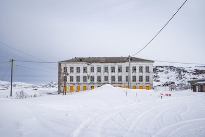 Snow covered field by buildings against sky