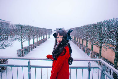 Portrait of young woman standing on snow covered railing