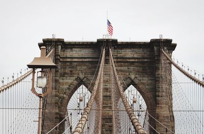 Suspension bridge in city against cloudy sky