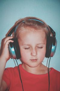 Boy with eyes closed listening music while standing against blue wall at home