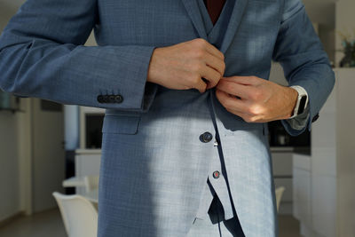 Midsection of businessman buttoning blazer at home