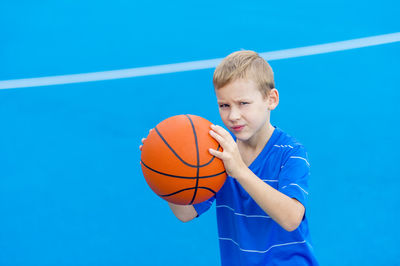 Portrait of boy holding basketball while standing on sports court