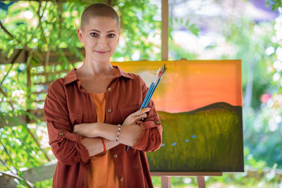 Beautiful young woman posing in front of her art canvas painting outdoors in her garden. 