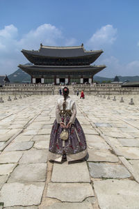 Back view of anonymous female wearing traditional dress standing on road leading to oriental shrine with curved roof in seoul