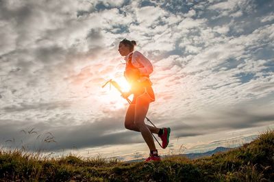 Low angle view of young woman jumping against sky during sunset