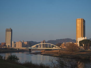 Bridge over river by buildings against clear sky