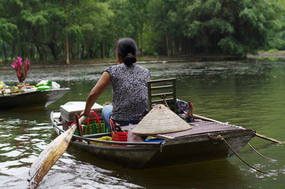 Rear view of man sitting on lake against trees