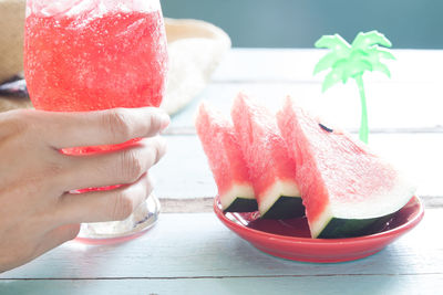 Cropped hand having watermelon drink on table