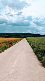 Empty road amidst field against sky