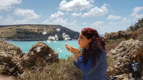 Side view of young woman blowing dandelion flowers on mountain