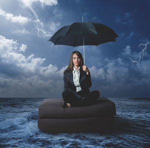 Young woman sitting on sea against sky