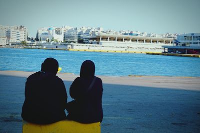 Rear view of people sitting on beach against clear sky