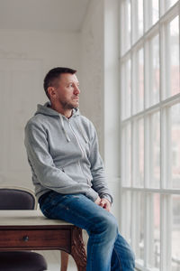 Man looking away while sitting on window