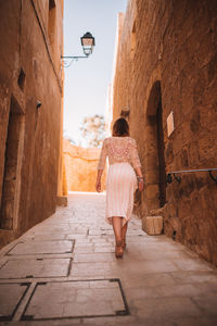 Rear view of woman walking on footpath amidst buildings