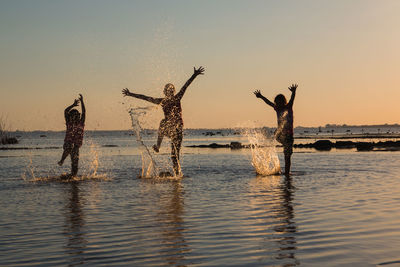 Silhouette people in sea against sky during sunset