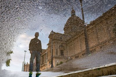 Man and big building reflected on puddle water in barcelona 