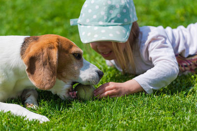 Happy little girl playing with beagle dog in garden.