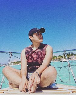 Man sitting by sea against clear blue sky