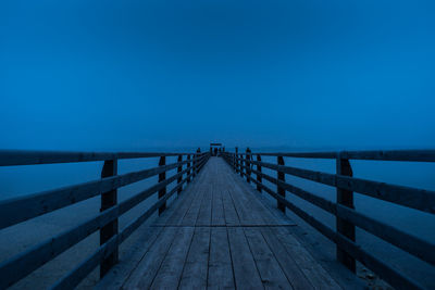 Footbridge over sea against clear blue sky