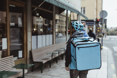 Rear view deliver man with backpack on sidewalk