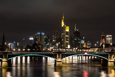 Illuminated arch bridge over river main in city against sky at night